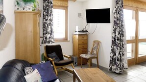 Una sala de estar con un sofá de cuero, una mesa de centro de madera, dos sillas, un televisor y un aparador.
