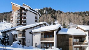 Un edificio cubierto de nieve con varios balcones y una pista de esquí al fondo.