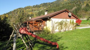 A wooden house with a red roof, a porch, and a slide in the foreground. - Kunzhof by Interhome (Treffen)
