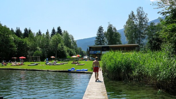 A wooden dock extending into a lake with boats and umbrellas on the shore. - Kunzhof by Interhome (Treffen)