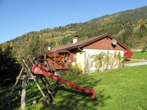 Situated in a lush valley, this chalet-style building offers a traditional retreat with a wooden porch and stairs.