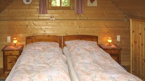 A double bed with floral bedding in a wooden cabin-style room with two bedside lamps. - Kunzhof by Interhome (Treffen)
