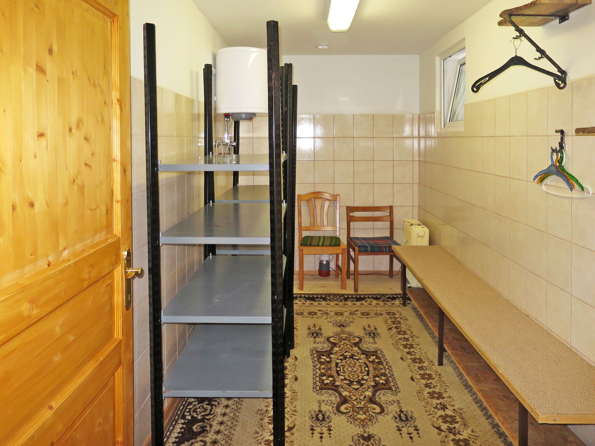 A compact kitchen with a wooden door, a metal shelf unit, a dining table, and a rug.