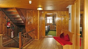 Un intérieur en bois avec un escalier, un banc doté de coussins rouges et une porte donnant sur une autre pièce.
