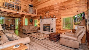 A cozy log cabin interior with a fireplace, leather sofas, and a dining area. - Cozy secluded cabin with firepit! - Absolutely Secluded (Gatlinburg)