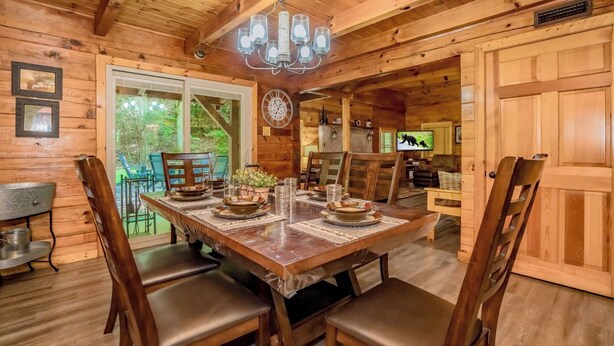 A wooden cabin interior with a dining table set for four, a chandelier, and a television in the background. - Cozy secluded cabin with firepit! - Absolutely Secluded (Gatlinburg)