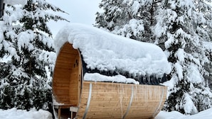 Una estructura de madera cubierta de nieve con techo curvo, rodeada de árboles cargados de nieve.