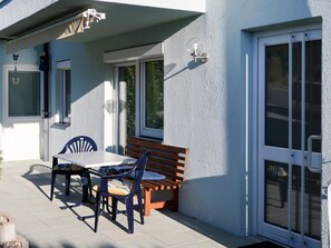 A patio with a table and chairs, a wooden bench, and a sliding glass door.