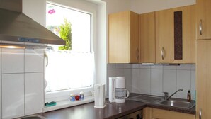 A kitchen with wooden cabinets, a stainless steel stove, a window with a view of greenery, and a coffee maker on the counter. - Apartment Frisch by Interhome (Imst)