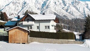 A two-story chalet with a wooden exterior and a snow-covered roof, set against a backdrop of snow-capped mountains. - Apartment Frisch by Interhome (Imst)