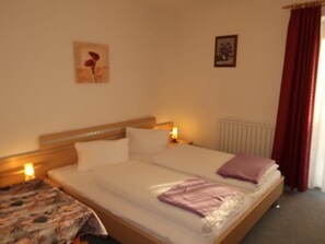 A hotel room with a bed, bedside tables, a radiator, and a window with curtains.