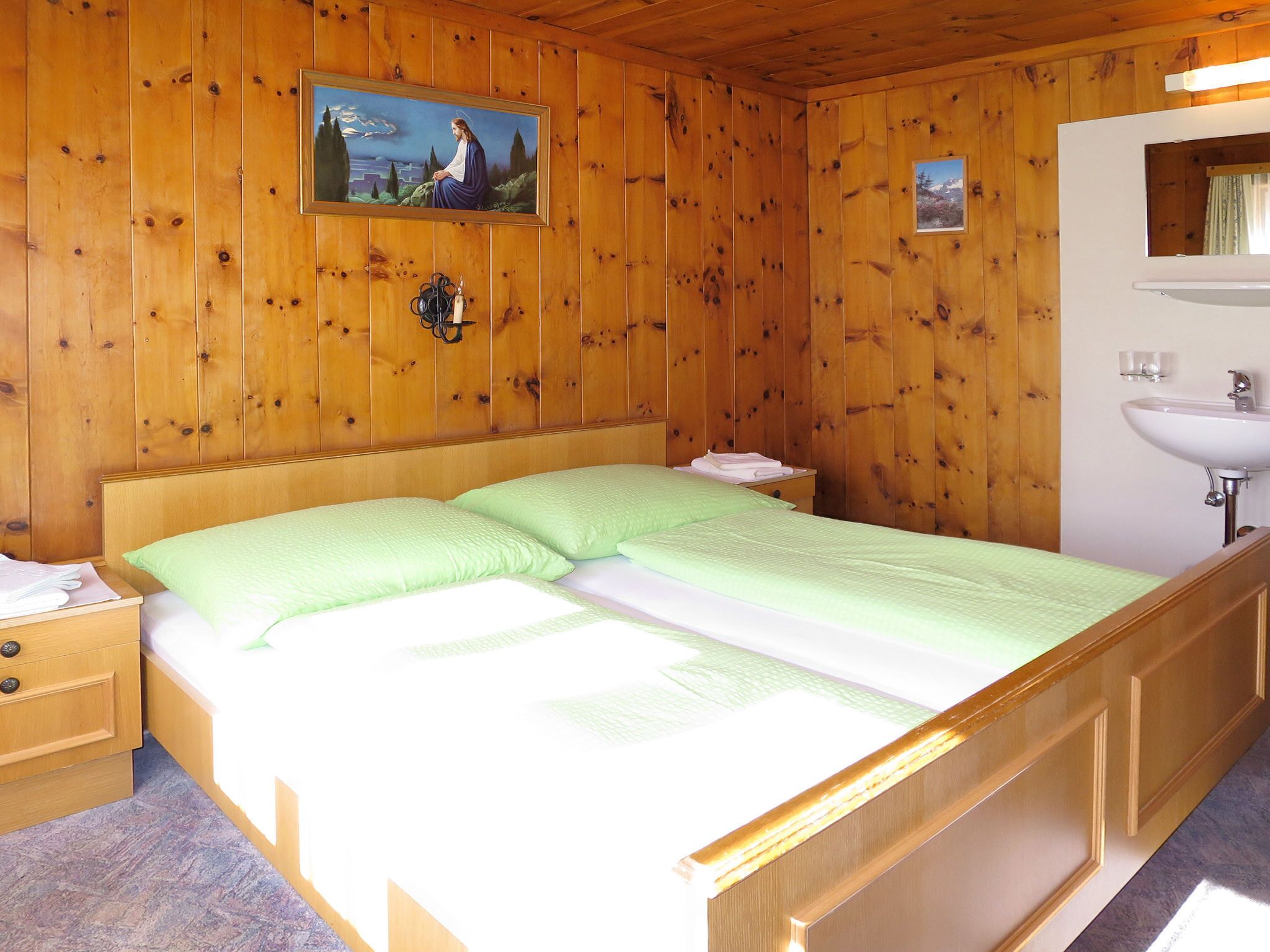 Een kamer met houten lambrisering, een bed, nachtkastje, een wandlamp en een klein raam.