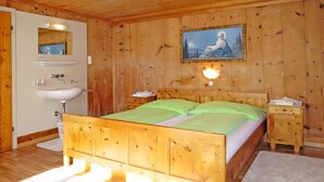 Une chambre aux murs lambrissés, comprenant un lit, une table de chevet, une lampe fixée au mur, un tableau, et une salle de bain avec un lavabo et un miroir.