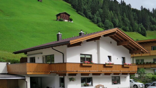 A two-story chalet with a balcony, a garage, and a view of a green hillside. - Haus Alina by Interhome (Tux)