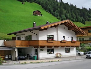 A two-story chalet with a balcony, a garage, and a view of a green hillside. - Haus Alina by Interhome (Tux)
