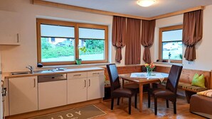 A compact kitchen with a dining area, wooden cabinets, a sink, and a window with curtains. - Haus Alina by Interhome (Tux)