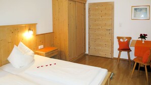 A hotel room with a wooden bed, a wooden wardrobe, a small table with a vase of flowers, and a wooden chair.