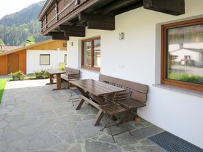 Relax in the outdoor seating area with wooden benches and tables on a stone-paved patio, surrounded by a beautiful view.