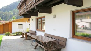 An outdoor patio with wooden benches and a stone floor, surrounded by white walls and wooden beams. - Elisabeth by Interhome (Zell am Ziller)