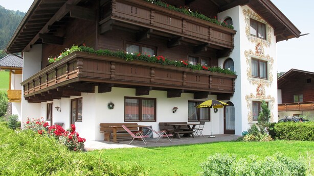 Un chalet à deux étages doté de balcons en bois, d’un patio couvert et d’un jardin.
