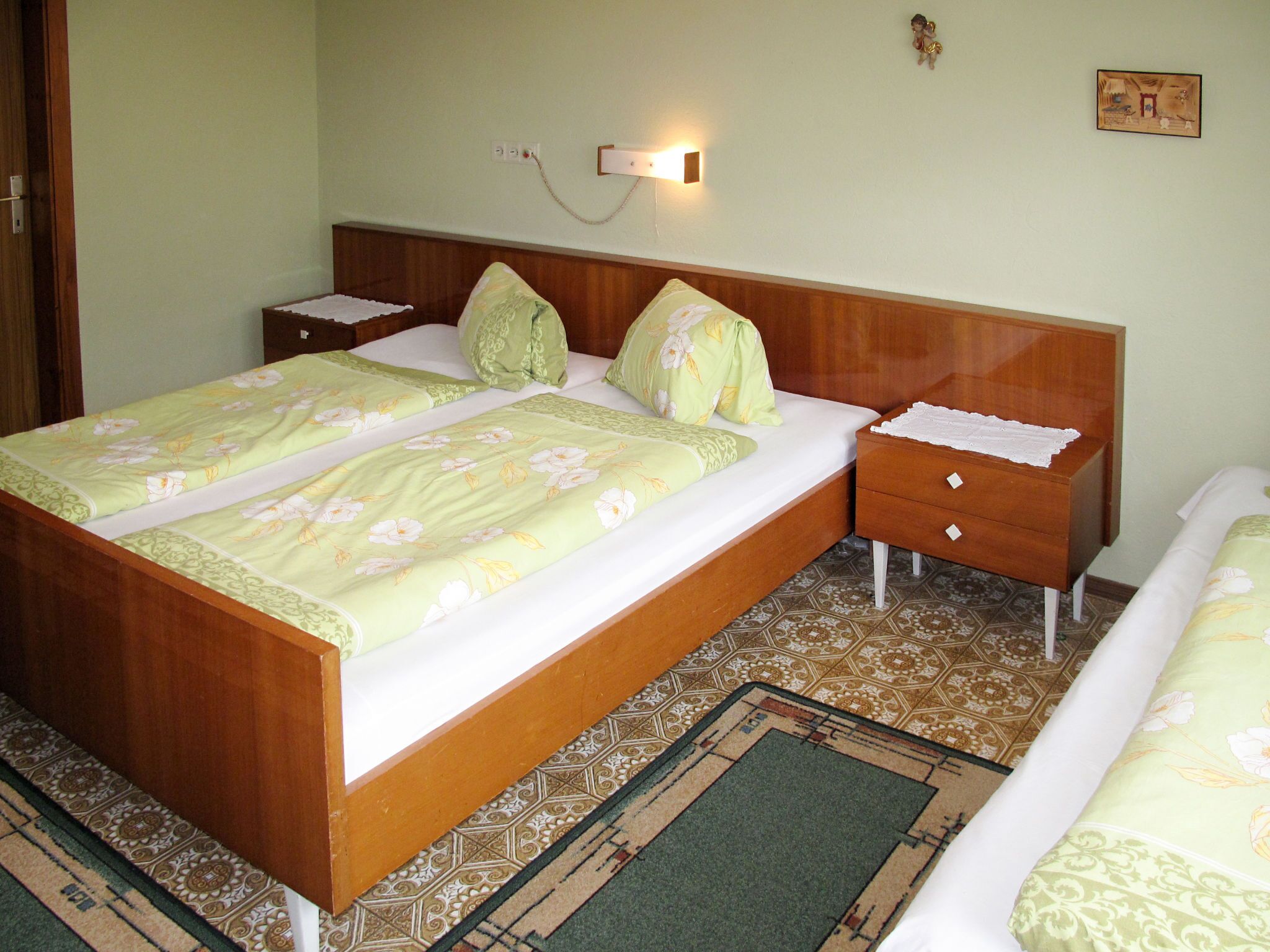 Ein Doppelbett mit floralem Bettzeug, ein Nachttisch mit Lampe und ein gemustertes Teppich.