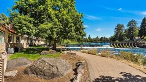 A riverside walkway with a wooden deck, large rocks, and a tree.