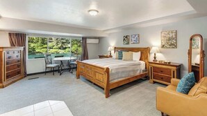 A bedroom with a wooden bed, bedside tables, a chair, a desk, and a large window with a view of greenery.