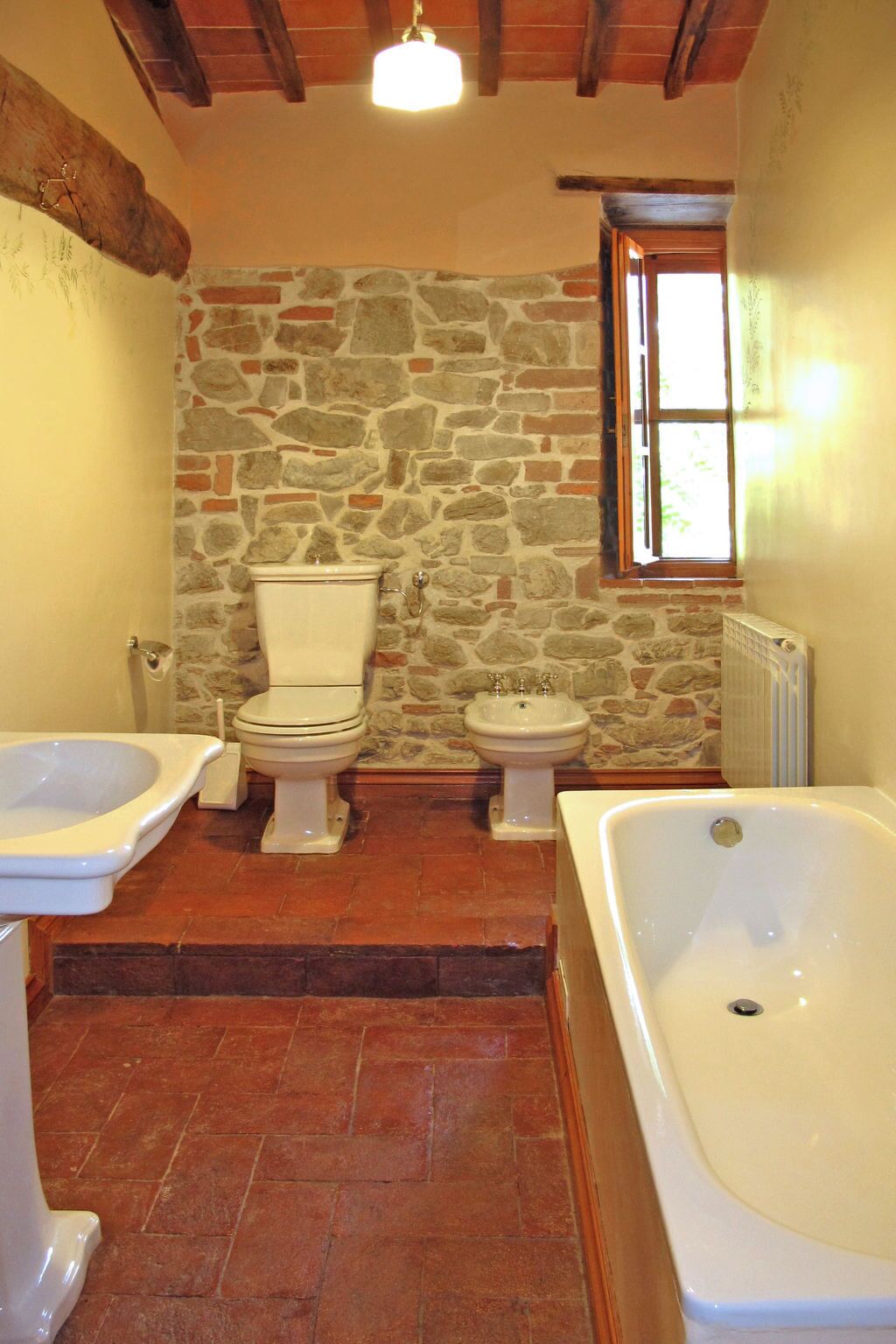 Ein Badezimmer mit Steinwand, Toilette, Bidet, Badewanne und Fenster.