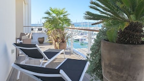 A balcony with two lounge chairs, a large potted plant, and a view of a marina with boats. - La Marina by Interhome (Scarlino)