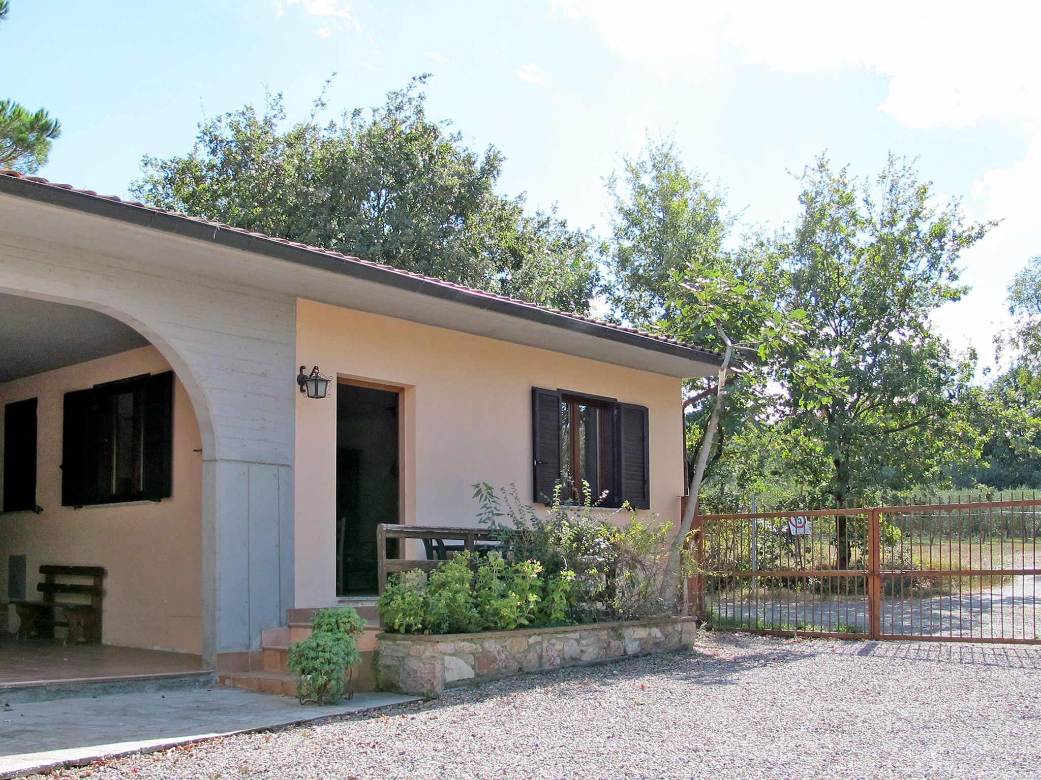 Ein eingeschossiges Haus mit überdachter Veranda, einem Garten mit Steinmauer und einem Metalltor.