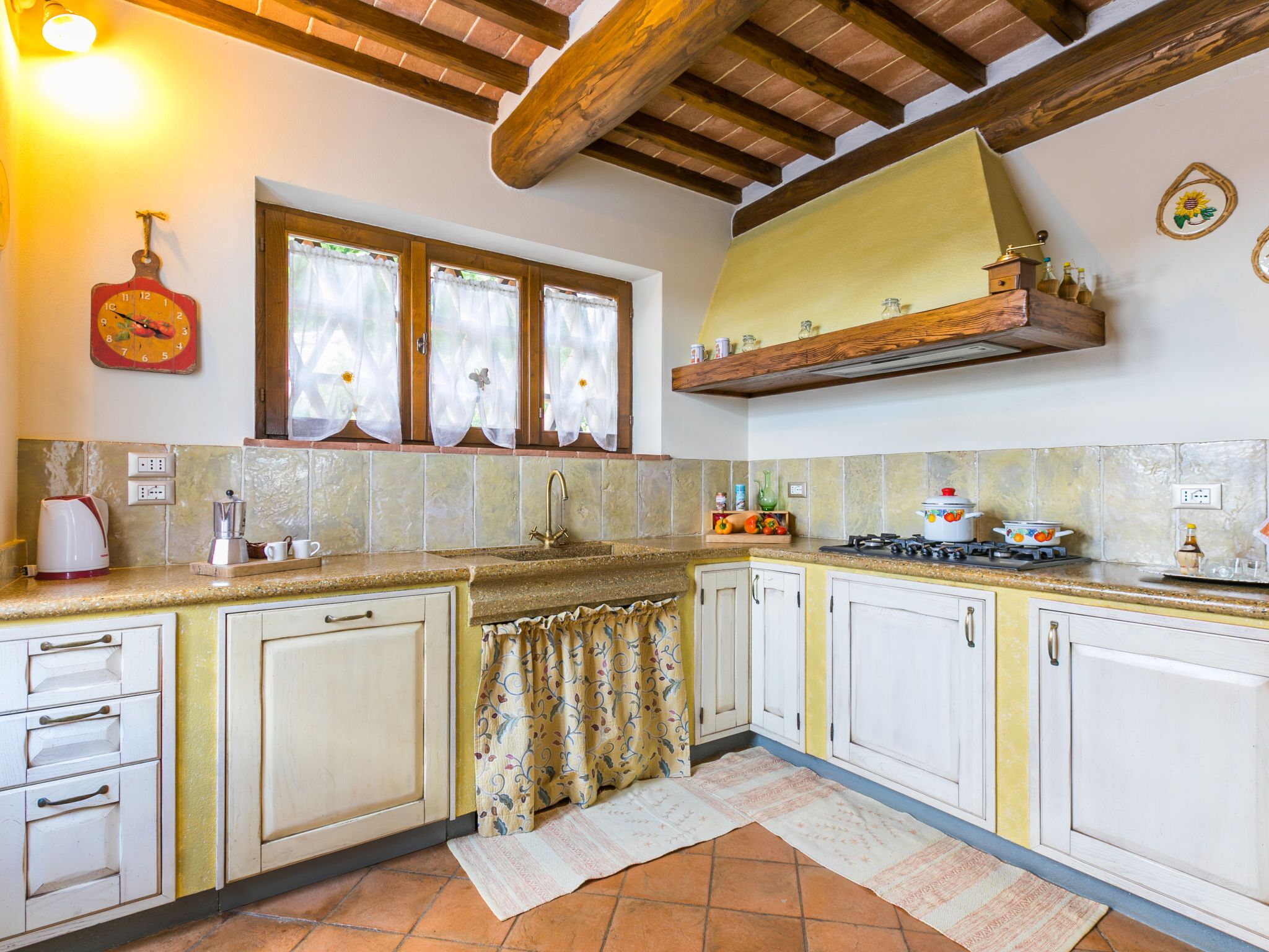 Une cuisine avec un mur recouvert de carreaux, des poutres apparentes en bois, une cuisinière à gaz et des armoires blanches.