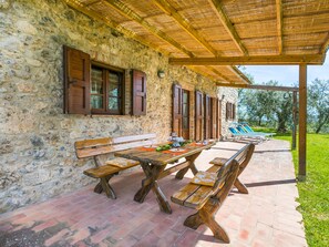 An outdoor patio with rustic stone walls, wooden benches, and a covered area with a thatched roof.