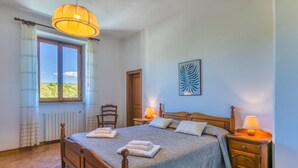 Een slaapkamer met een houten bed, twee bedlampen, een radiator, een stoel en een raam met gordijnen.
