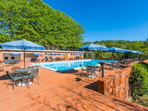 Een zwembadterras met een zwembad, blauwe parasols en buitenmeubilair.