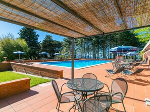 Relax by the clear pool surrounded by a patio, lounge chairs, and umbrellas, under a shaded bamboo pergola.
