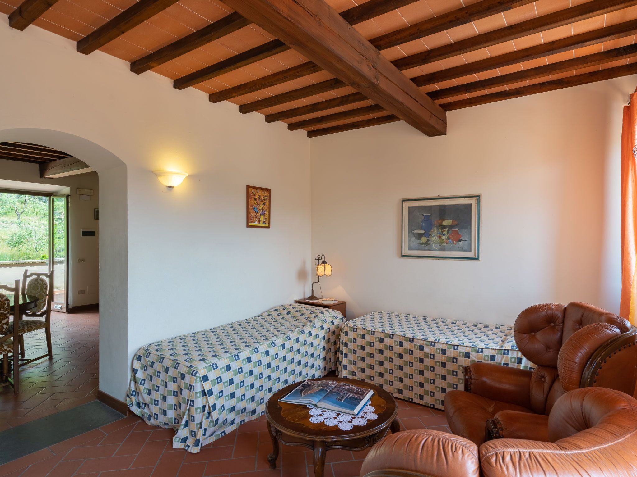 Una habitación con dos camas, un sofá de cuero, una mesita con un libro y un cuadro en la pared.