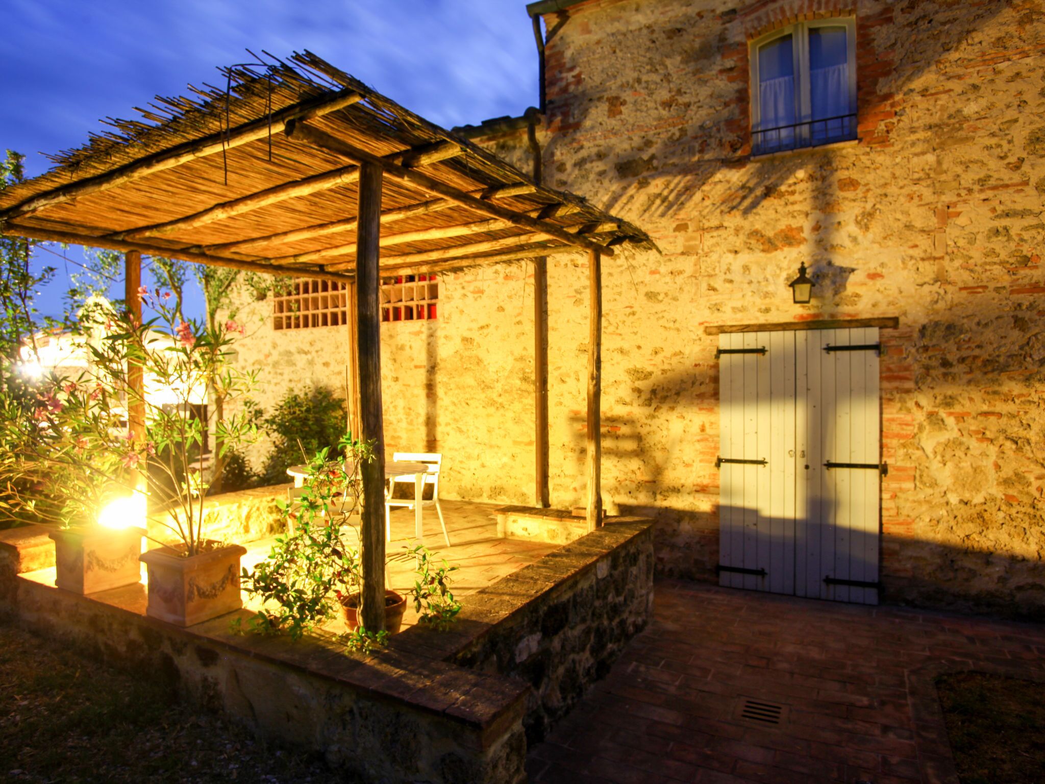 Un edificio rústico de piedra con una pérgola de madera y una puerta blanca.