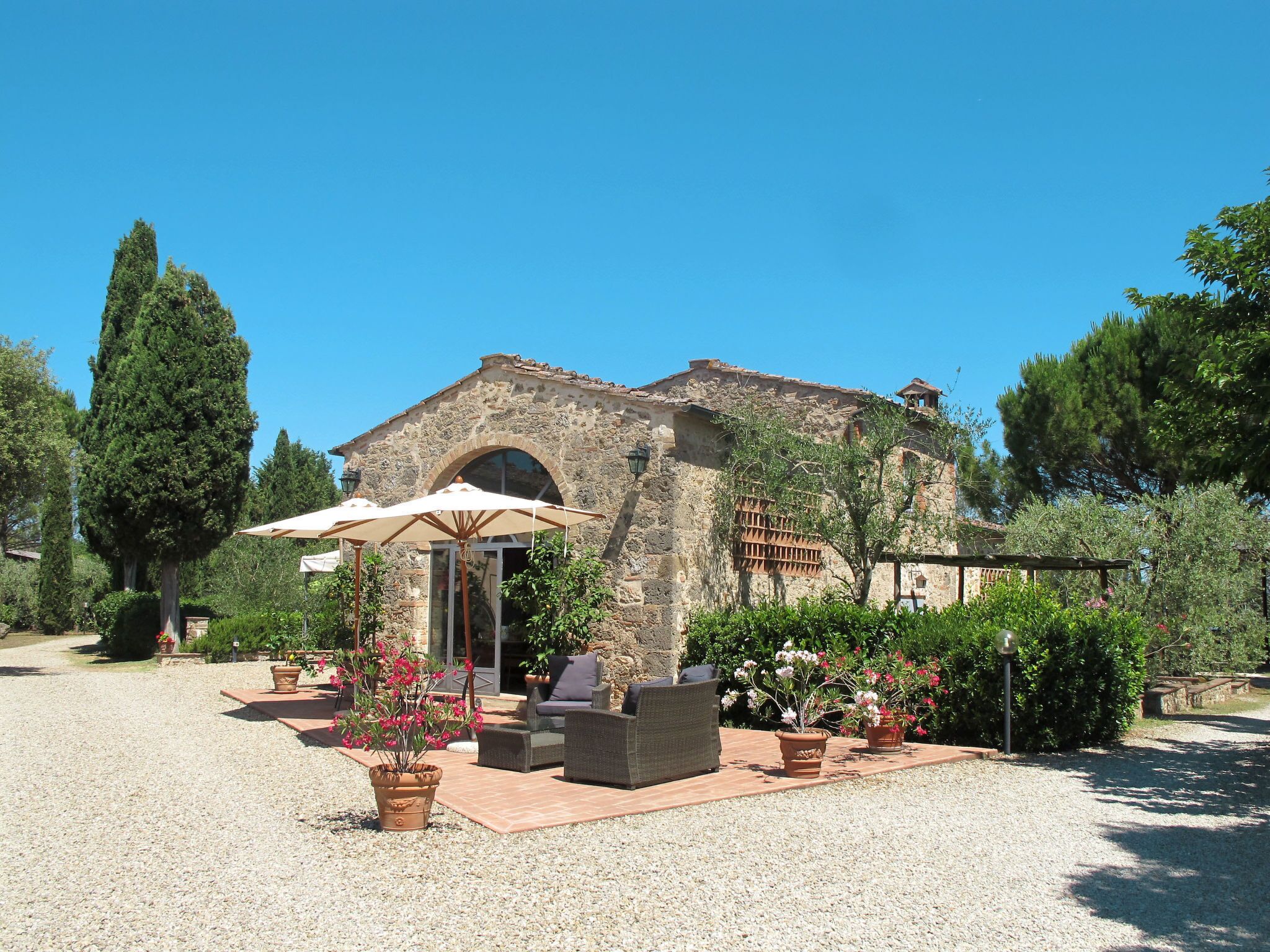 A rustic stone building with a large arched entrance, outdoor seating area with wicker furniture, and potted plants.