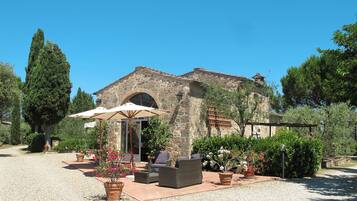 A rustic stone building with a large arched entrance, outdoor seating area with wicker furniture, and potted plants.