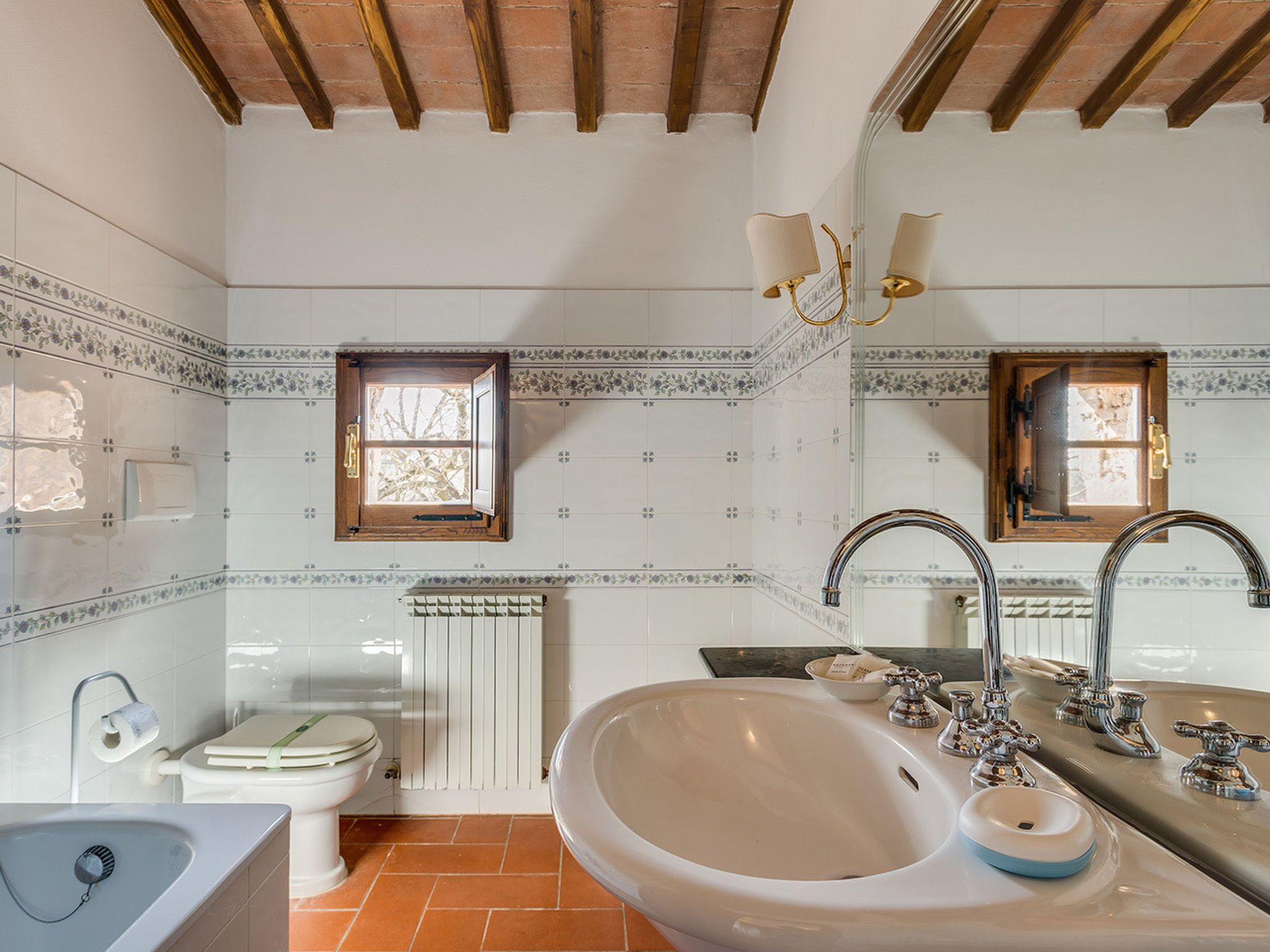 Une salle de bain avec un grand lavabo, deux miroirs, des toilettes et une fenêtre.