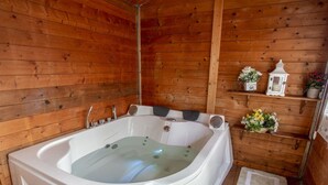 Une cabane en bois dotée d’un bain à remous, de murs en bois et d’une petite étagère où sont disposés des objets décoratifs.