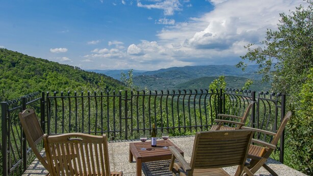 Une terrasse avec des chaises et une table en bois, d’où l’on peut admirer un paysage montagneux.