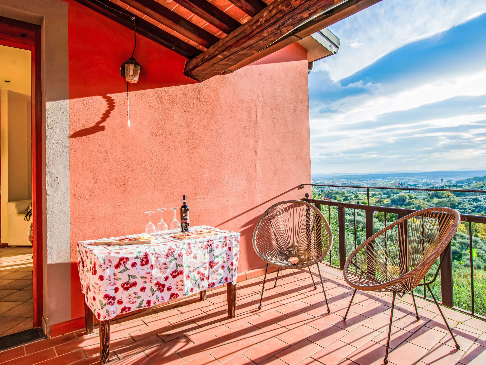A balcony with a table and chairs, a bottle of wine, and a view of the countryside.