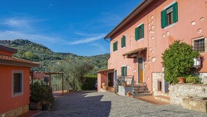 A courtyard with cobblestone paving, a pink building with green shutters, and a tree. - Francesco by Interhome (Montecatini Terme)