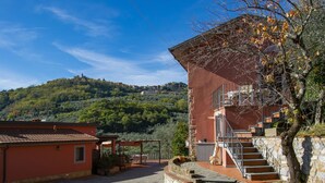 A courtyard with a red building, stone steps, and a view of a hillside with buildings. - Francesco by Interhome (Montecatini Terme)
