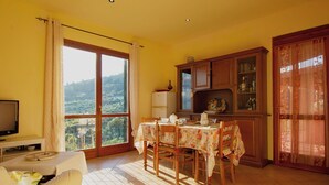 A dining area with a table set for four, a television on a stand, and a view of a mountainous landscape through a large window. - Francesco by Interhome (Montecatini Terme)