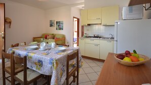 A compact kitchen with a dining area, featuring a table set for four, a fruit basket, and a stove. - Villaggio Le Palme by Interhome (Lignano Pineta)