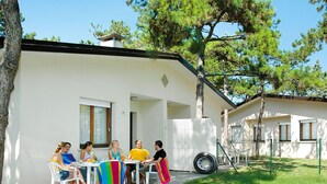 A group of people seated at an outdoor table with a white fence and trees in the background. - Villaggio Le Palme by Interhome (Lignano Pineta)
