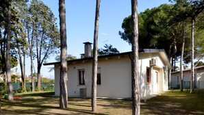 A small, single-story building with a flat roof, surrounded by tall trees and a grassy area. - Villaggio Le Palme by Interhome (Lignano Pineta)