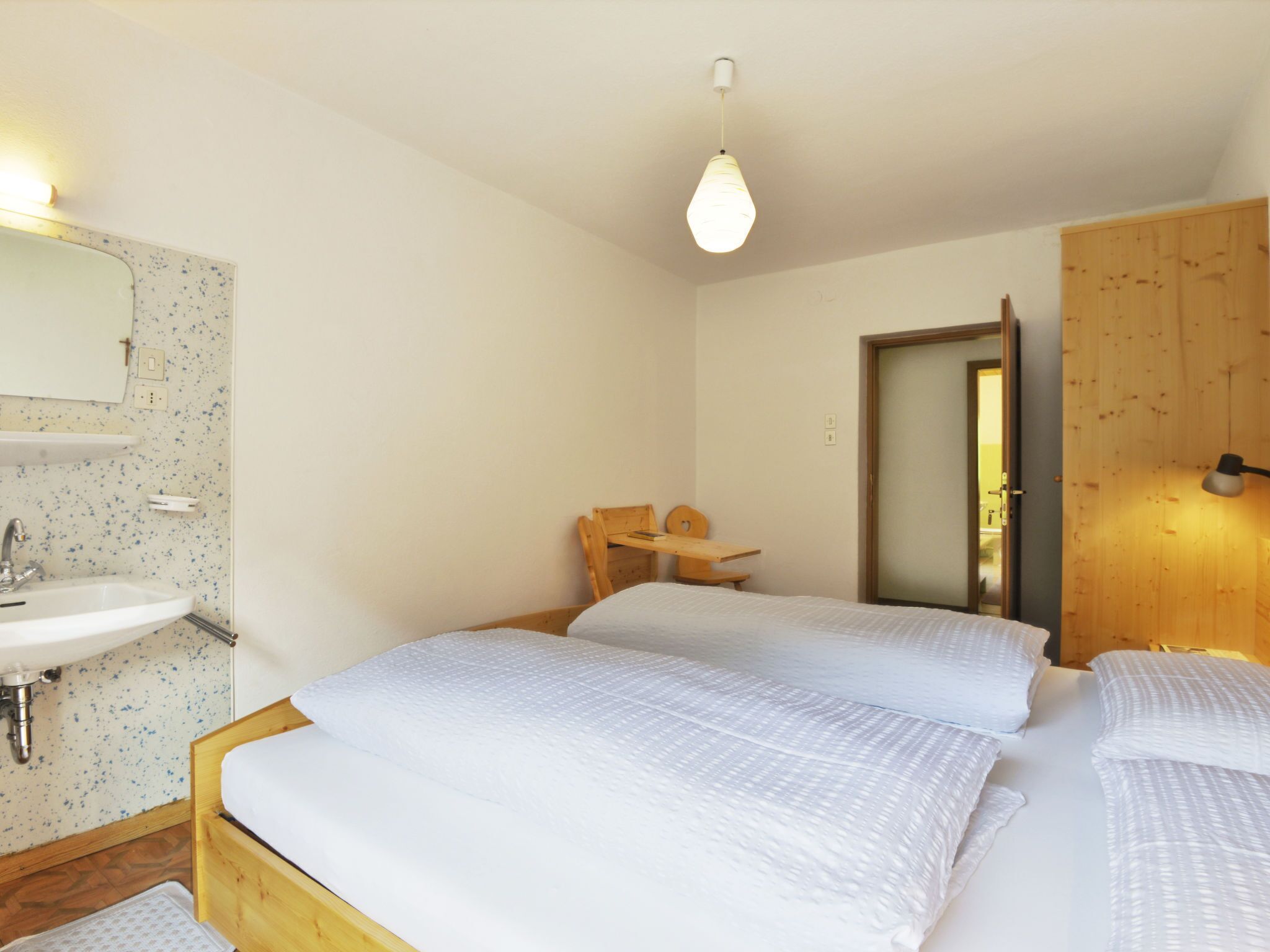Una camera da letto con due letti, una scrivania in legno, uno specchio e un lavandino.
